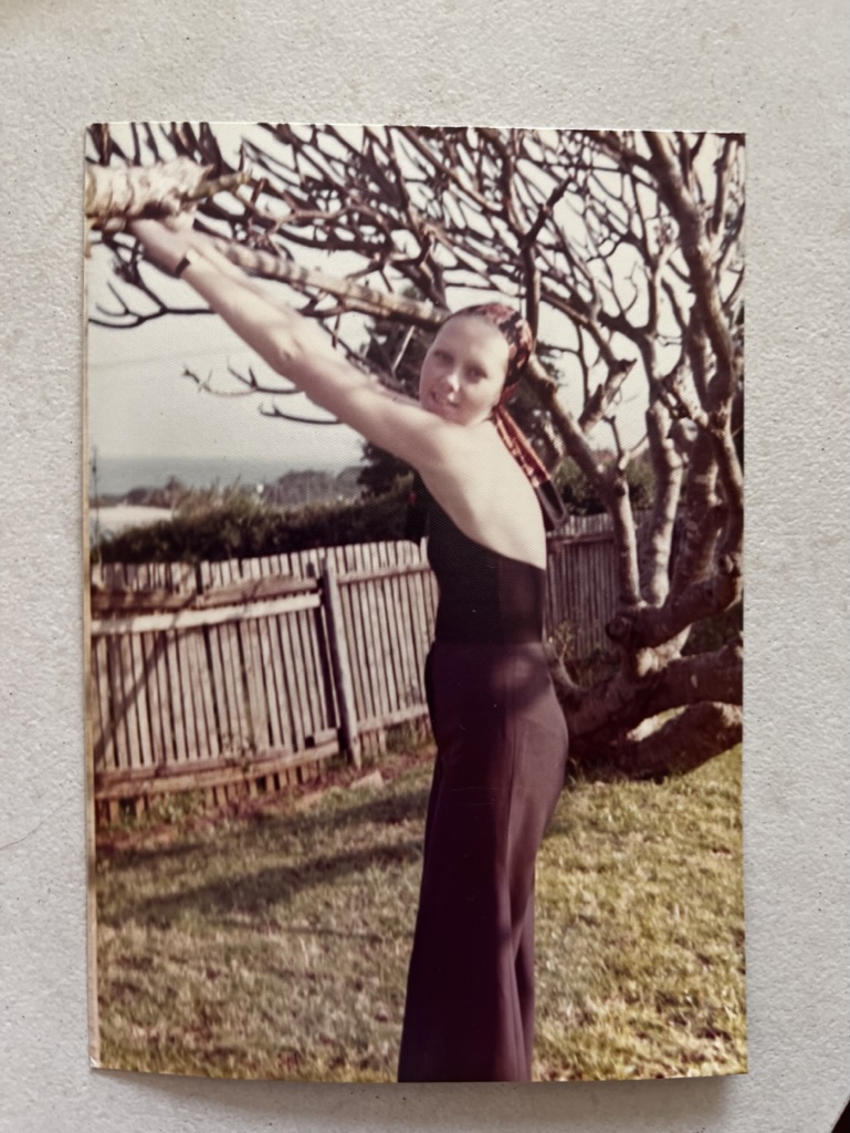 Vintage photograph of a woman posing outdoors beside a leafless tree in a garden